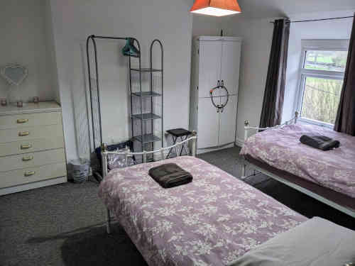 showing two single beds, chest of drawers and storage rack with spare blankets