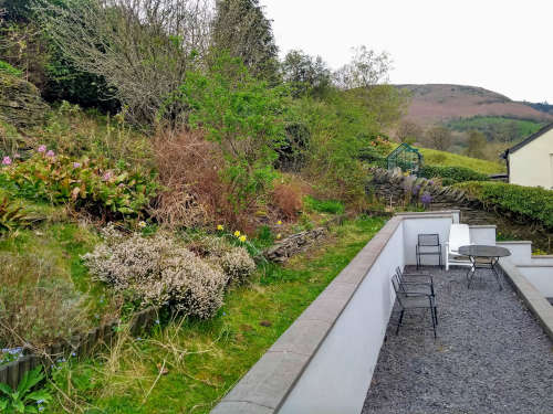 The rear garden at Jasmine Cottage, with outdoor tables, chairs and sunlounger and views of Llantysilio tramway in the distance.